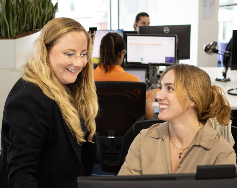 Two women chatting and looking over a screen in an office