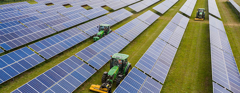 Aerial view of the Lightsource bp Maen Hir Solar and Energy Storage project in the UK, part of their UK Projects portfolio, tractors maintain grass between rows of solar panels.