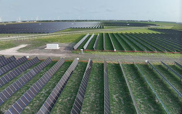 Aerial view of the Lightsource bp Peacock solar project in Texas, part of their US Projects portfolio, rows of solar panels stretch across green fields with wind turbines visible in the distance.