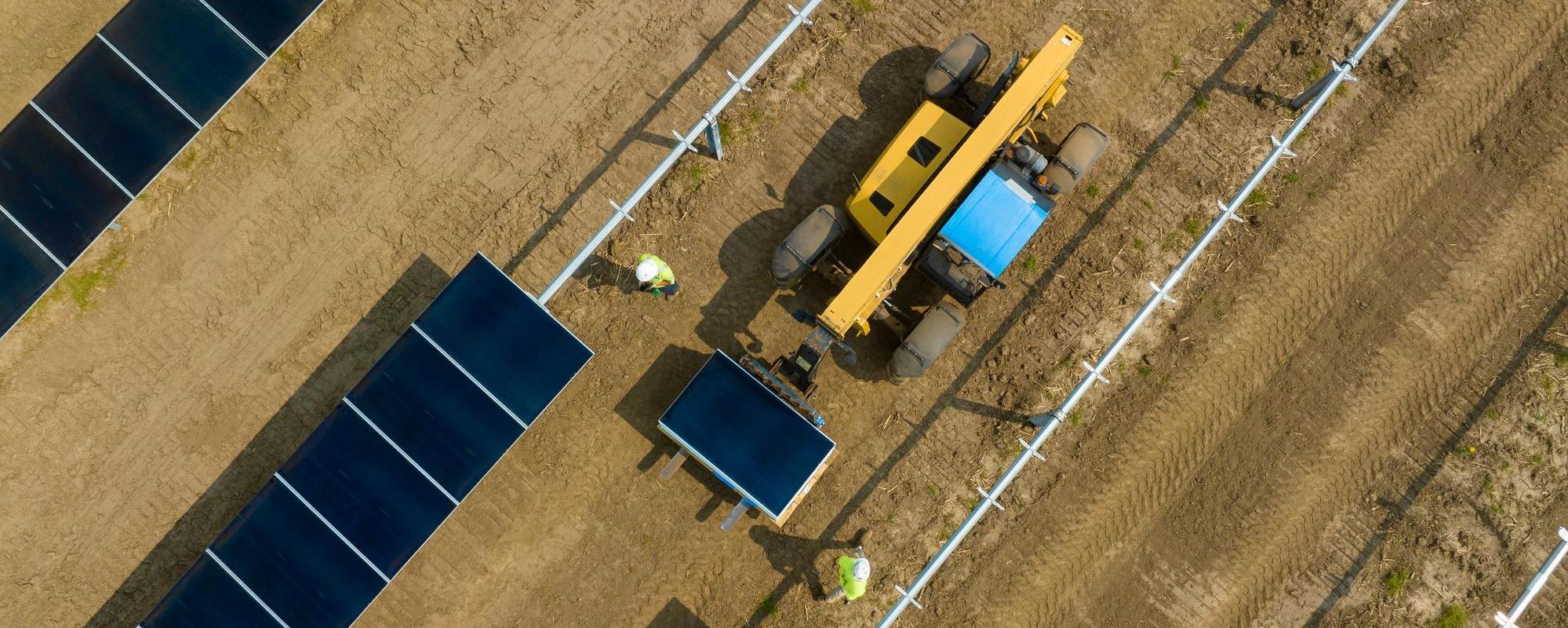 Aerial shot of construction workers and machinery building rows of solar panels