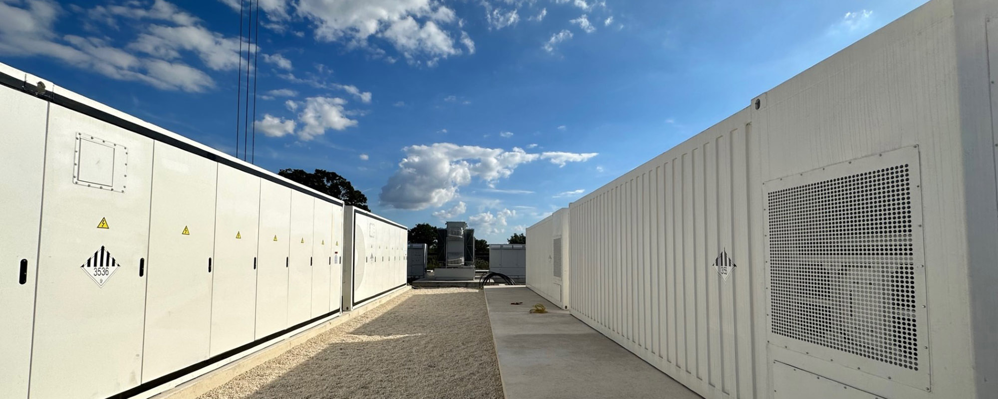 Rows of white battery storage containers at a Lightsource bp solar project, set against a bright blue sky with scattered clouds.